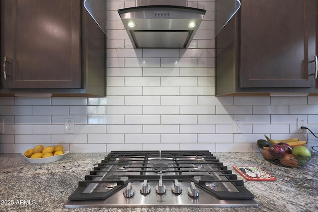 kitchen with backsplash, dark brown cabinetry, island exhaust hood, dark stone counters, and stainless steel gas stovetop