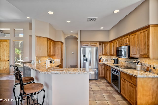 kitchen featuring light stone counters, tasteful backsplash, kitchen peninsula, a breakfast bar, and appliances with stainless steel finishes