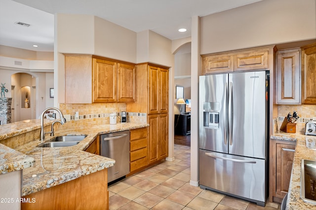 kitchen featuring stainless steel appliances, light stone countertops, light tile patterned floors, sink, and backsplash