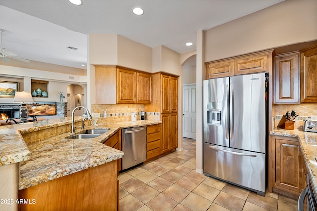 kitchen featuring stainless steel appliances, sink, tasteful backsplash, kitchen peninsula, and light stone countertops