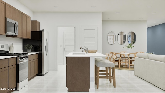 kitchen with a breakfast bar, light countertops, appliances with stainless steel finishes, a sink, and an island with sink