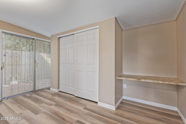 unfurnished bedroom featuring access to outside, a closet, baseboards, and wood finished floors