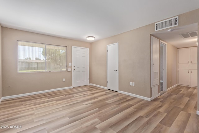 spare room featuring light wood-type flooring, visible vents, and baseboards