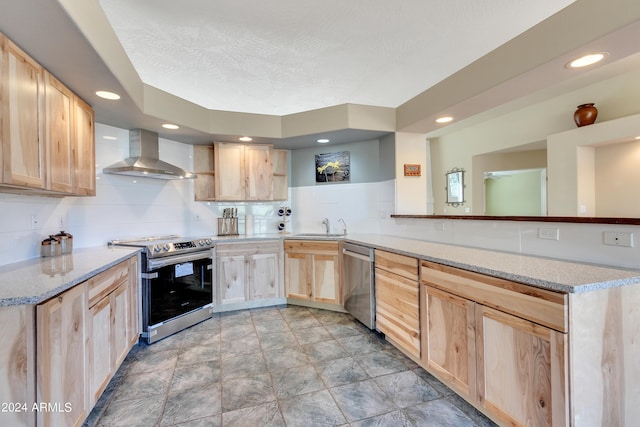 kitchen featuring appliances with stainless steel finishes, wall chimney exhaust hood, light brown cabinetry, and kitchen peninsula