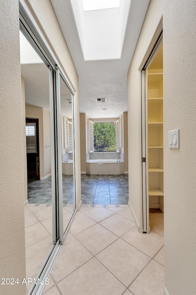 hallway featuring a skylight, plenty of natural light, and light tile patterned floors