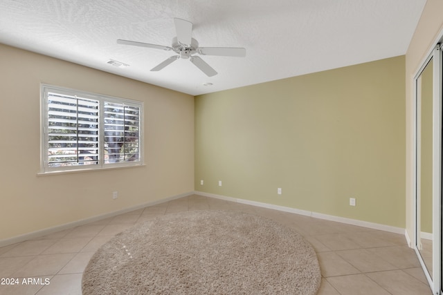 spare room featuring a textured ceiling, ceiling fan, and light tile patterned floors