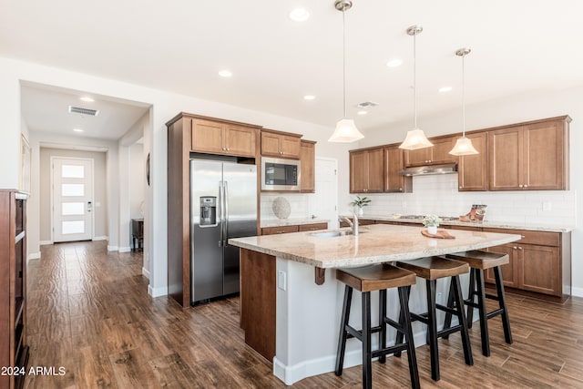 kitchen featuring a kitchen island with sink, pendant lighting, dark wood-type flooring, light stone counters, and stainless steel appliances