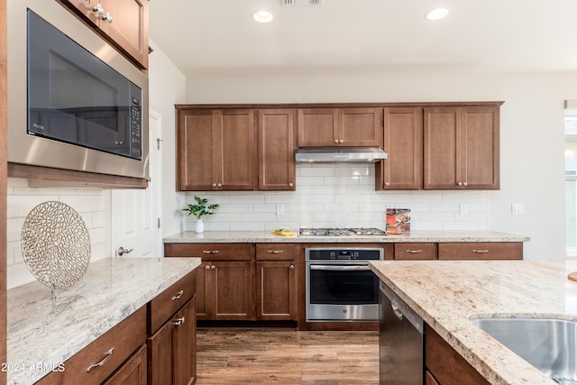 kitchen featuring light stone countertops, backsplash, appliances with stainless steel finishes, and light wood-type flooring