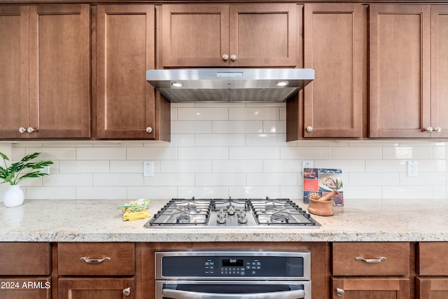 kitchen with light stone counters, exhaust hood, appliances with stainless steel finishes, and decorative backsplash