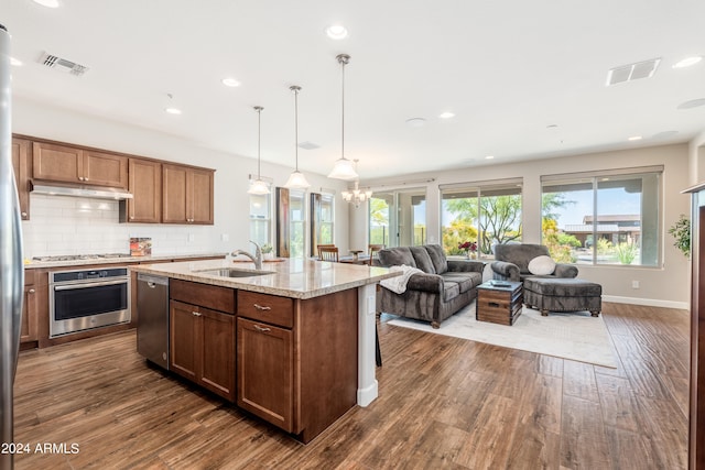 kitchen with light stone counters, sink, a center island with sink, dark wood-type flooring, and stainless steel appliances