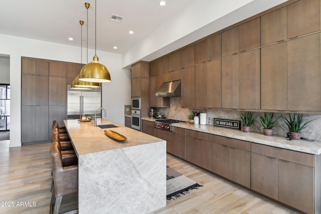 kitchen featuring a large island, sink, built in appliances, tasteful backsplash, and decorative light fixtures