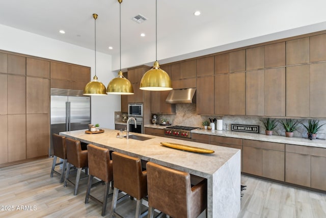 kitchen with sink, built in appliances, a kitchen breakfast bar, pendant lighting, and decorative backsplash