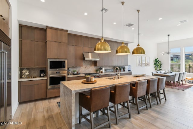 kitchen with built in microwave, sink, tasteful backsplash, stainless steel oven, and decorative light fixtures