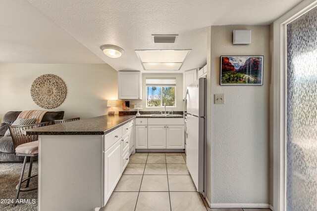 kitchen with kitchen peninsula, a kitchen breakfast bar, white refrigerator, and white cabinets