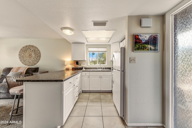 kitchen featuring dark countertops, freestanding refrigerator, a peninsula, a kitchen bar, and a sink