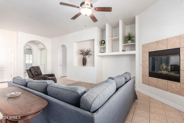 tiled living room with ceiling fan, built in features, and a tile fireplace