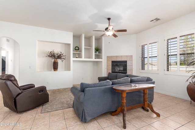 tiled living room with a tiled fireplace and ceiling fan