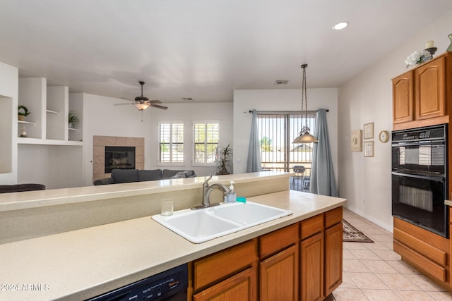 kitchen with a tile fireplace, black appliances, sink, hanging light fixtures, and ceiling fan