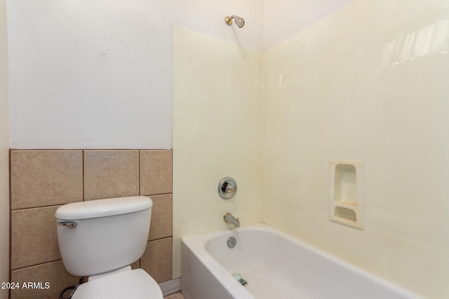 bathroom featuring shower / bathing tub combination, toilet, and tile walls