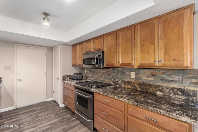 kitchen featuring decorative backsplash, appliances with stainless steel finishes, dark hardwood / wood-style floors, and dark stone counters