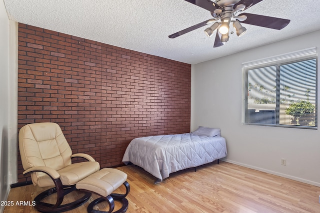 bedroom featuring ceiling fan, light wood-type flooring, brick wall, and a textured ceiling