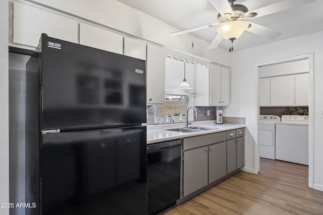 kitchen featuring washer and clothes dryer, black appliances, wood-type flooring, sink, and gray cabinets