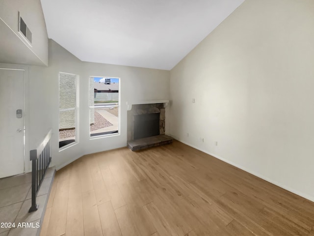 unfurnished living room featuring light hardwood / wood-style floors, vaulted ceiling, and a stone fireplace