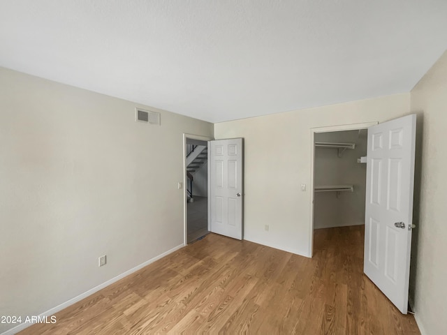 unfurnished bedroom with light hardwood / wood-style flooring, a spacious closet, and a closet