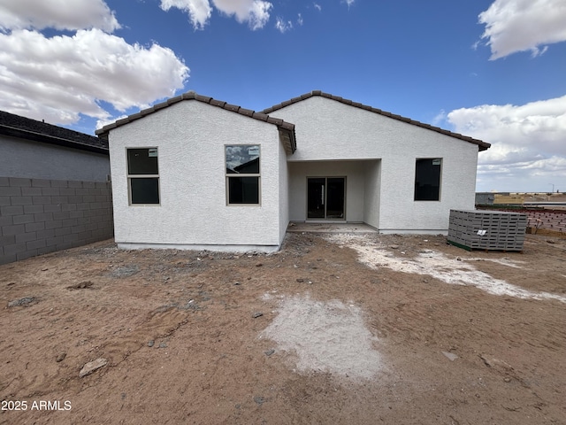 rear view of property featuring a tiled roof, fence, and stucco siding