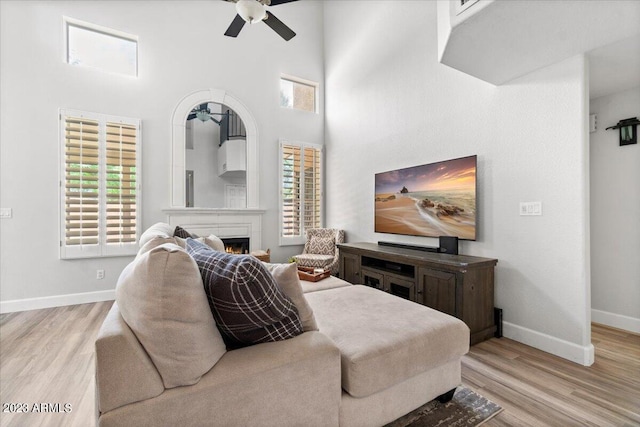 living room with light hardwood / wood-style floors, a high ceiling, plenty of natural light, and ceiling fan