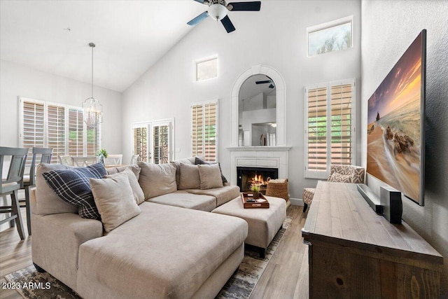 living room featuring high vaulted ceiling, light hardwood / wood-style flooring, and ceiling fan with notable chandelier