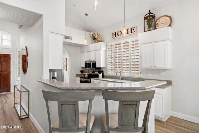 kitchen with hanging light fixtures, appliances with stainless steel finishes, light wood-type flooring, and white cabinets