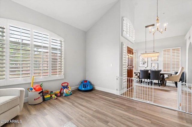 playroom with hardwood / wood-style floors, high vaulted ceiling, and an inviting chandelier