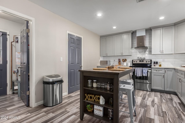 kitchen with gray cabinets, stainless steel range with electric cooktop, wall chimney range hood, backsplash, and hardwood / wood-style floors