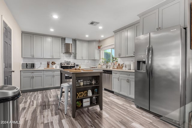 kitchen featuring backsplash, wall chimney range hood, gray cabinets, appliances with stainless steel finishes, and light wood-type flooring