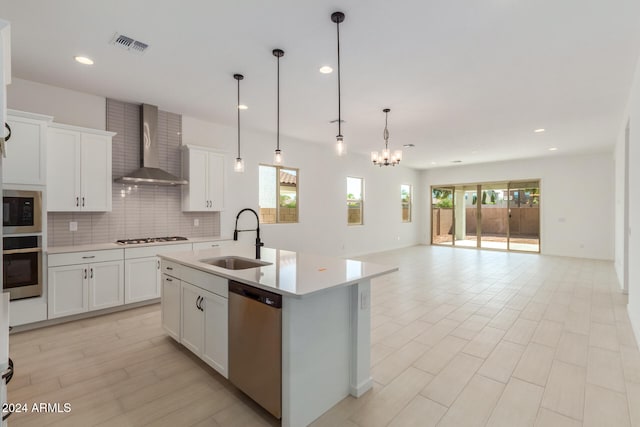 kitchen featuring sink, wall chimney exhaust hood, a center island with sink, white cabinets, and appliances with stainless steel finishes