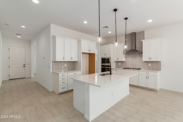 kitchen with pendant lighting, white cabinets, wall chimney exhaust hood, an island with sink, and stainless steel appliances