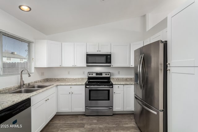 kitchen with sink, white cabinets, appliances with stainless steel finishes, and vaulted ceiling