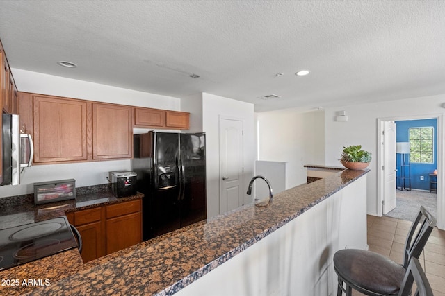 1350 S Greenfield Rd Unit 2133, Mesa, AZ 85206 - kitchen featuring black appliances, recessed lighting, a textured ceiling, brown cabinets, and dark stone counters