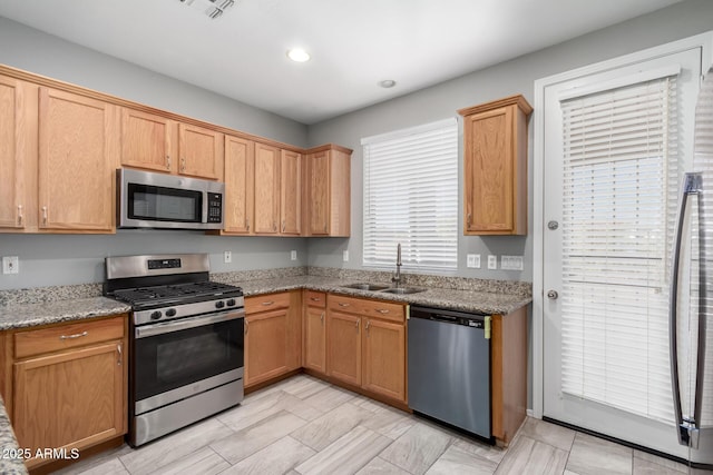 kitchen featuring appliances with stainless steel finishes, sink, and light stone counters