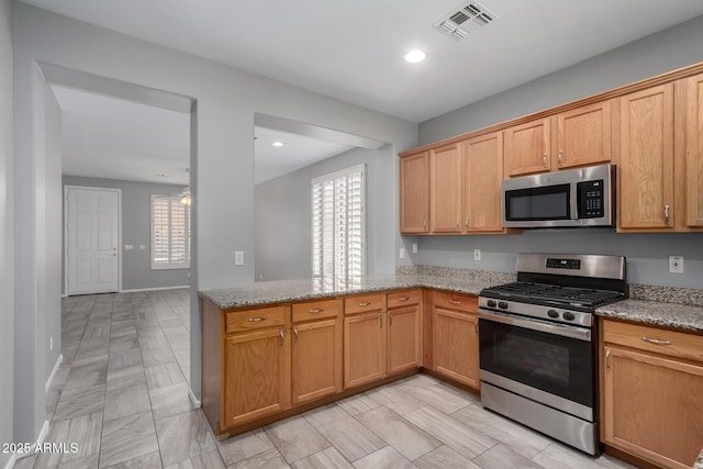 kitchen with appliances with stainless steel finishes, light stone countertops, and kitchen peninsula