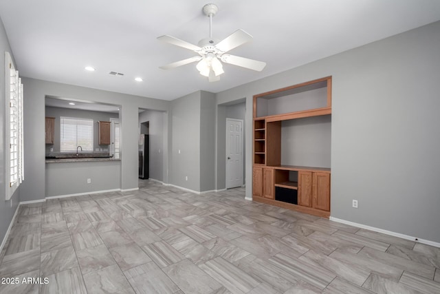 unfurnished living room with sink, built in features, and ceiling fan