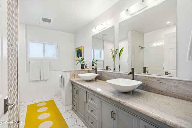 bathroom featuring tile flooring, tile walls, and dual bowl vanity