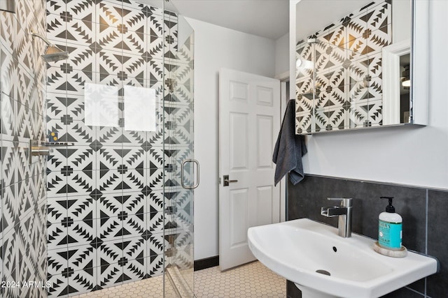 bathroom with tile walls, tile flooring, a shower with shower door, and sink