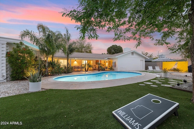 pool at dusk featuring a patio and a lawn