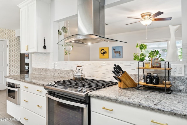 kitchen with ceiling fan, backsplash, island exhaust hood, gas stove, and white cabinets