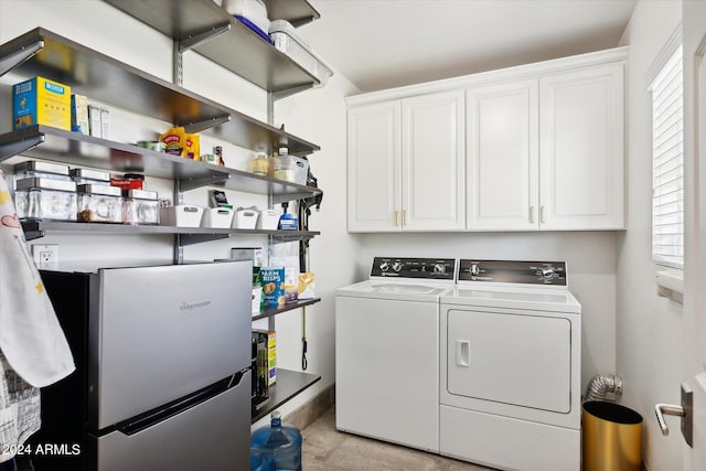 clothes washing area featuring light tile flooring, a healthy amount of sunlight, washing machine and dryer, and cabinets