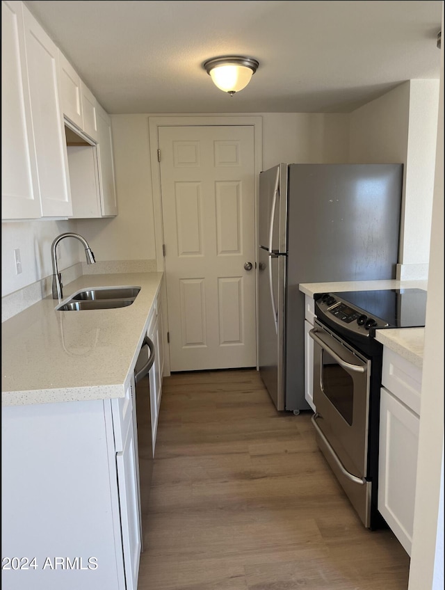 kitchen featuring appliances with stainless steel finishes, white cabinetry, light stone countertops, light wood-type flooring, and sink