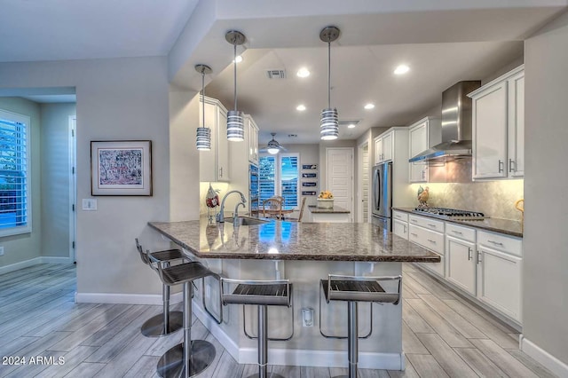 kitchen featuring stainless steel appliances, wall chimney range hood, wood finish floors, and visible vents