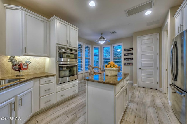 kitchen featuring stone counters, stainless steel appliances, a kitchen island, visible vents, and wood tiled floor